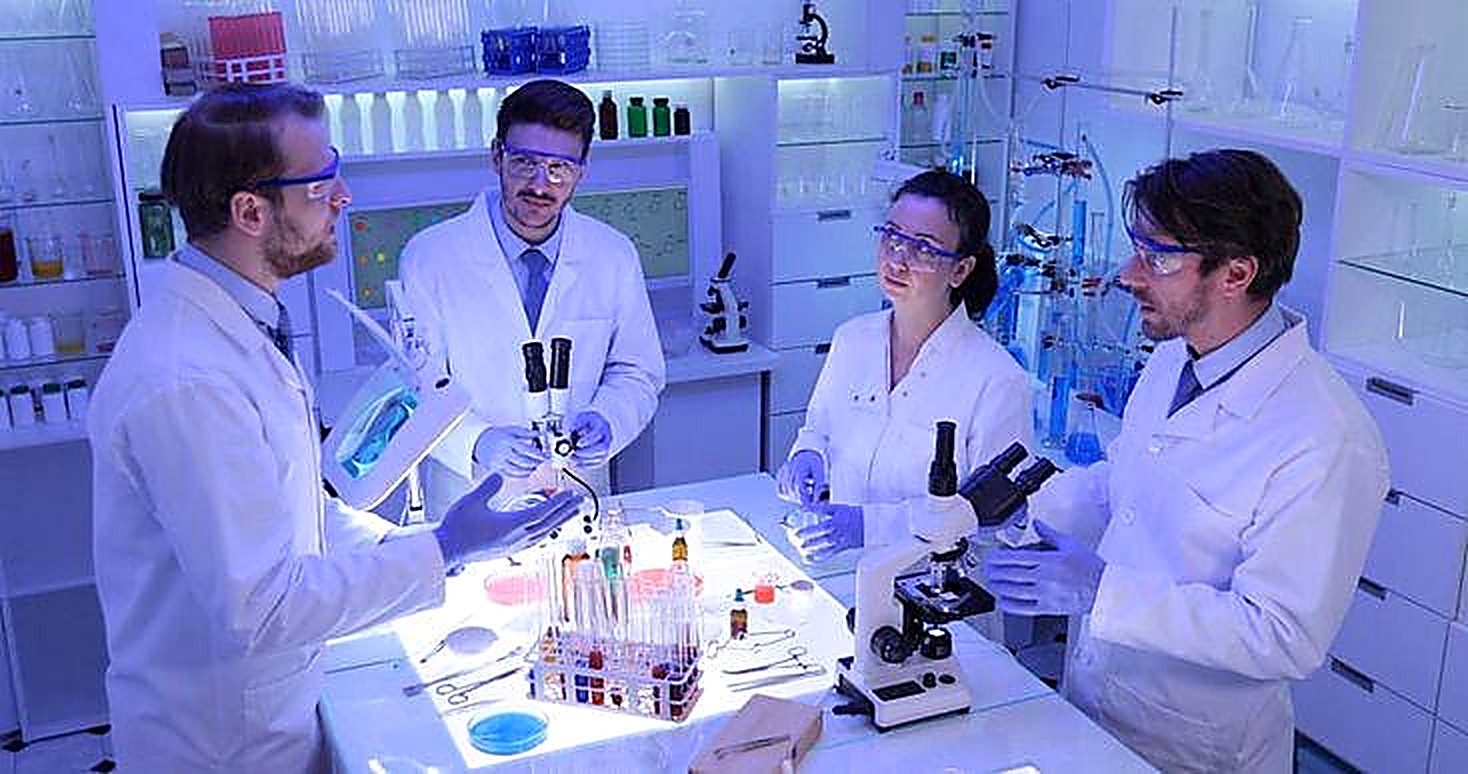 Scientists in lab coats reviewing samples and instrumentation together in a laboratory